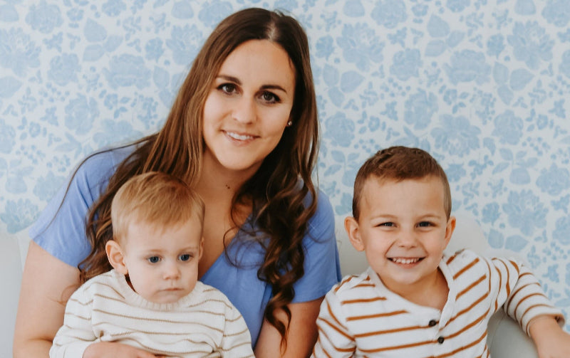Woman in a blue dress sitting on a white couch with two children against a blue patterned wall.
